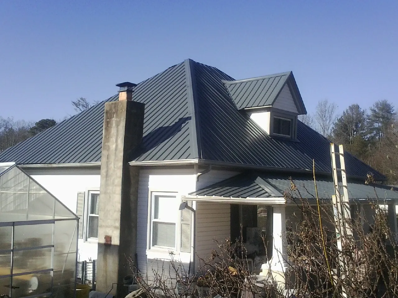 Dark blue standing seam metal roof on a white farmhouse with dormer — Slate & Tile Roof Repair by Roofing Brothers in Ozark