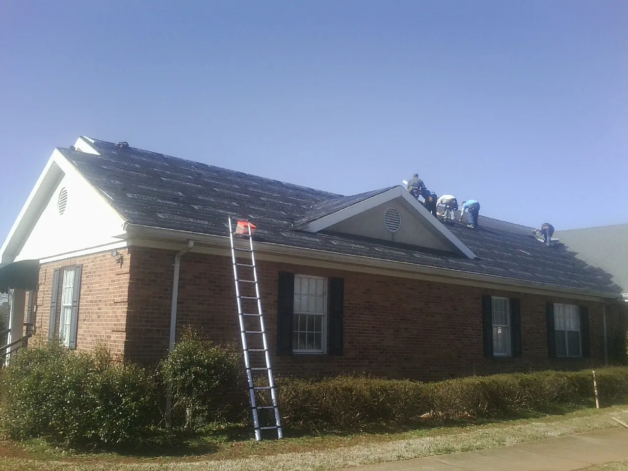 Crew tearing shingles off a brick ranch roof with a ladder set — Metal Roof Repair work by our crew in Ozark