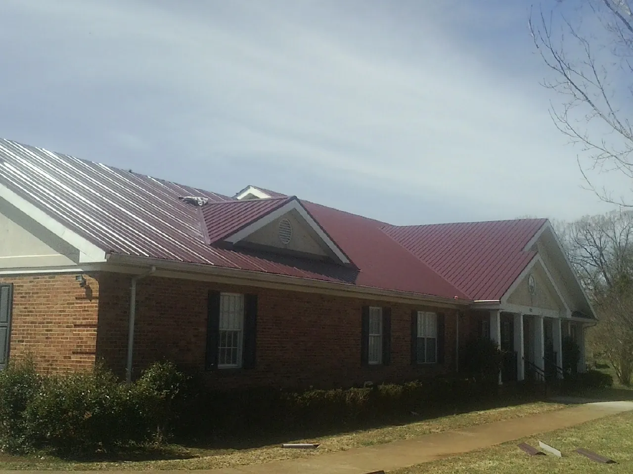 Red metal roof with gabled entries on a long brick building, from a Hail Damage Roof Repair job in Ozark