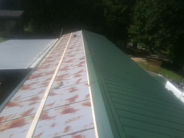 Old rusted panels beside newly installed green metal roofing — Wind Damage Roof Repair by Roofing Brothers in Ozark