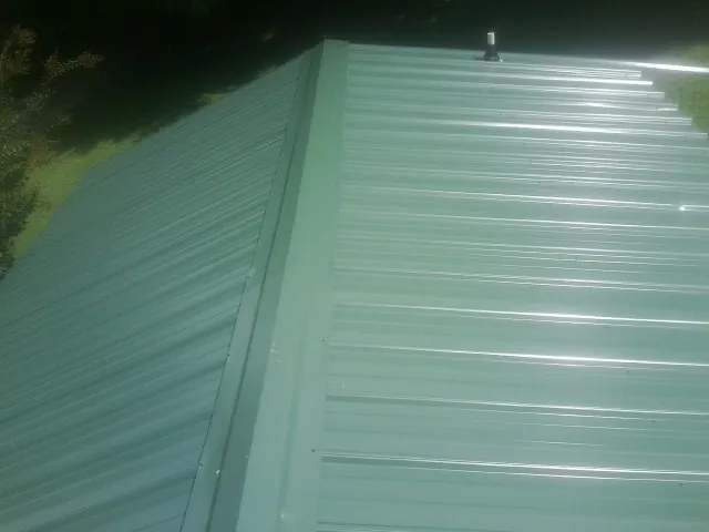 New green metal panels meeting at the ridge of a roof — Flat Roof Repair work by our crew in Ozark