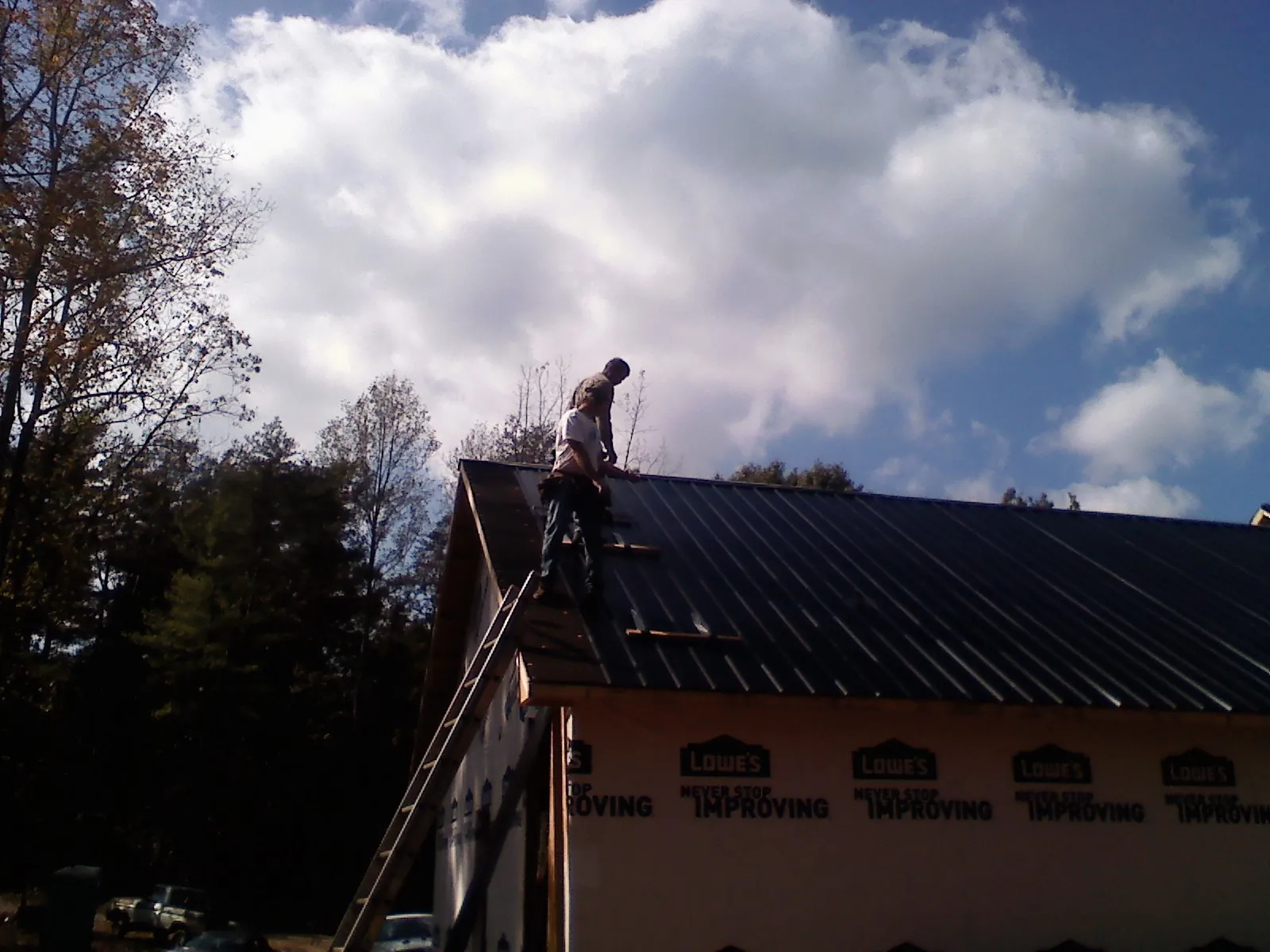 Roofer fastening dark metal panels high against a cloudy sky, from a Roof Inspection job in Ozark