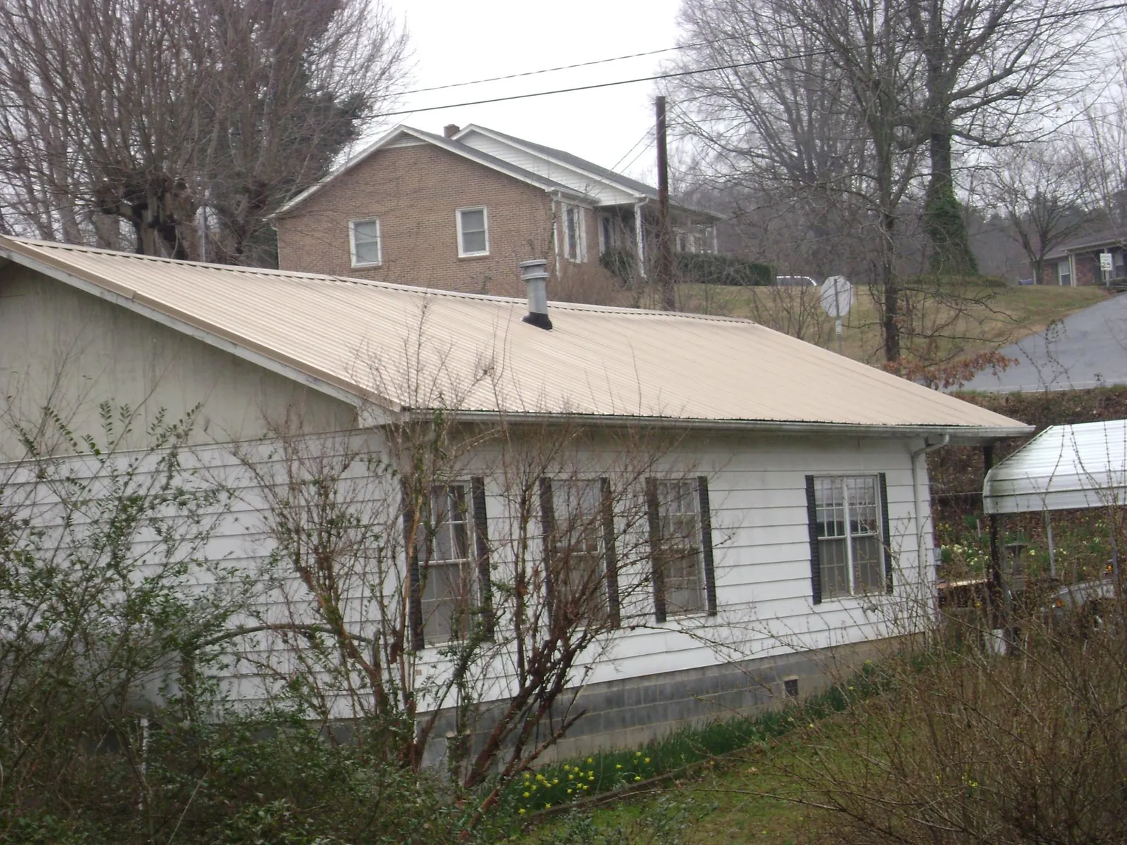 Tan metal roof on a white sided house set into a hillside — Commercial Roofing by Roofing Brothers in Ozark