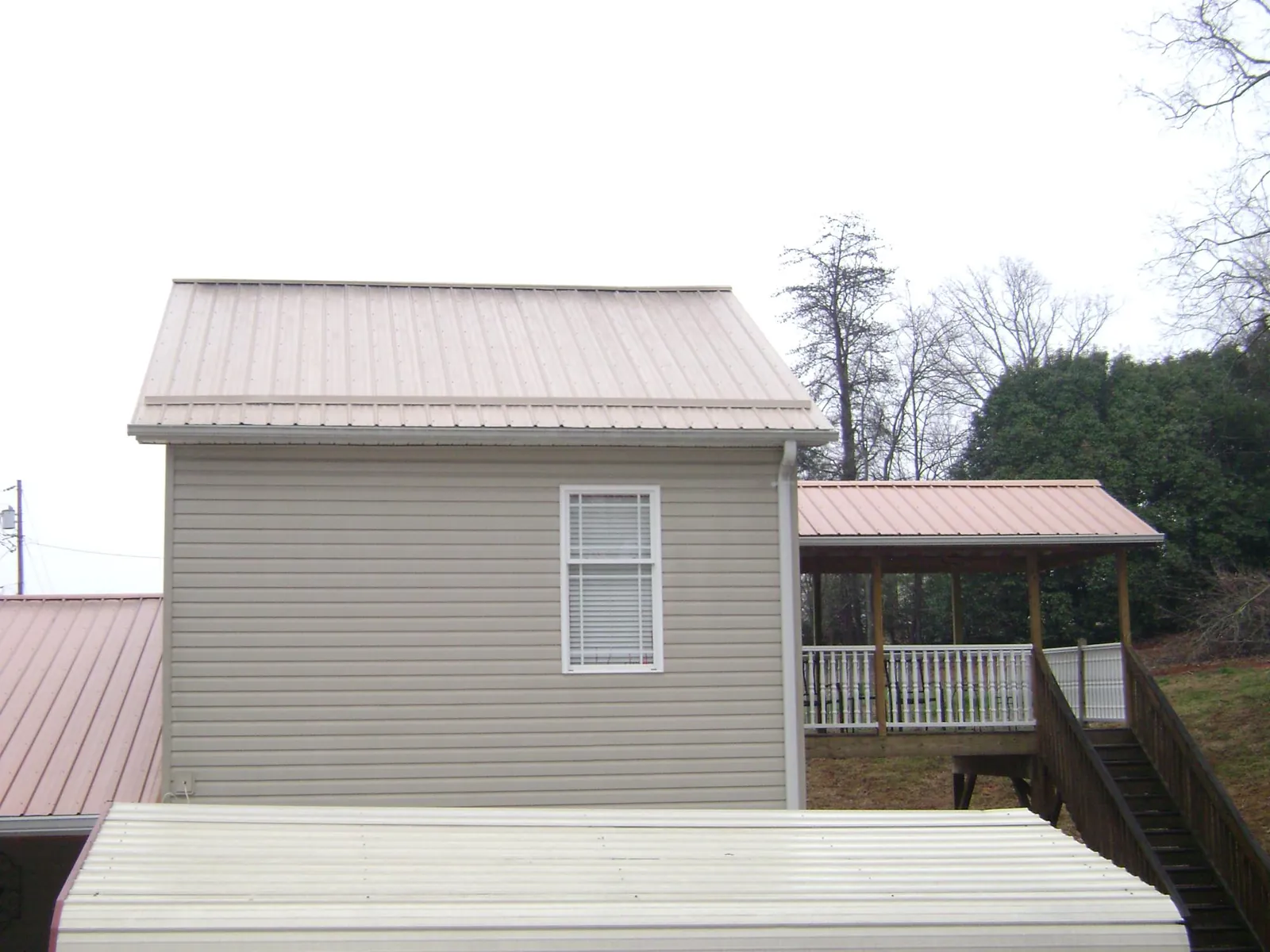 Tan metal roofs on a two story addition and attached porch, from a Roof Replacement job in Ozark