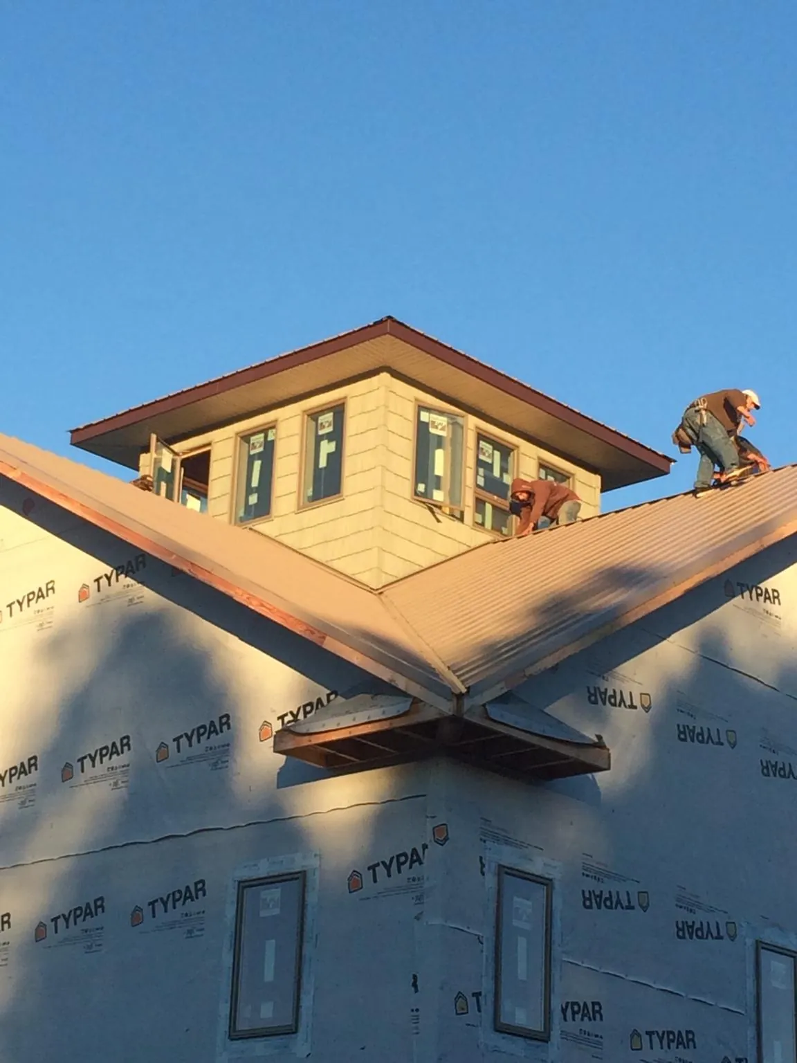 Roofers working around a rooftop cupola on a new metal roof at sunset — Roof Waterproofing in Ozark by Roofing Brothers